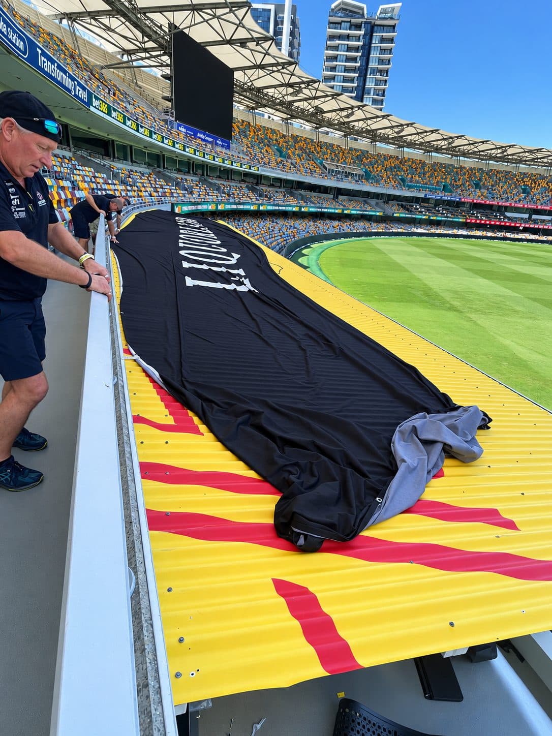 Crew installing a printed fabric banner along a stadium boundary fence