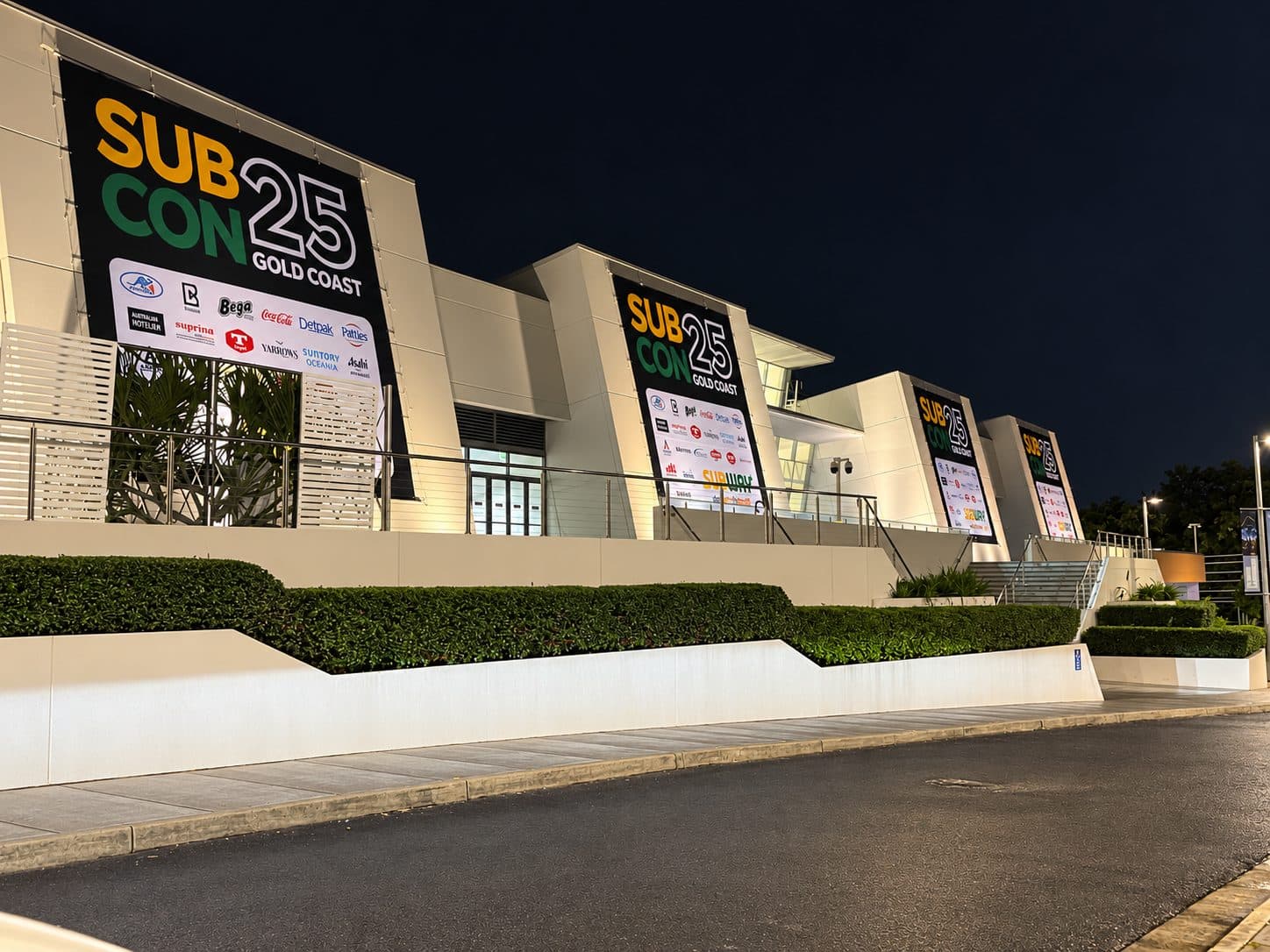 Four building banners lit up on a convention centre facade at night